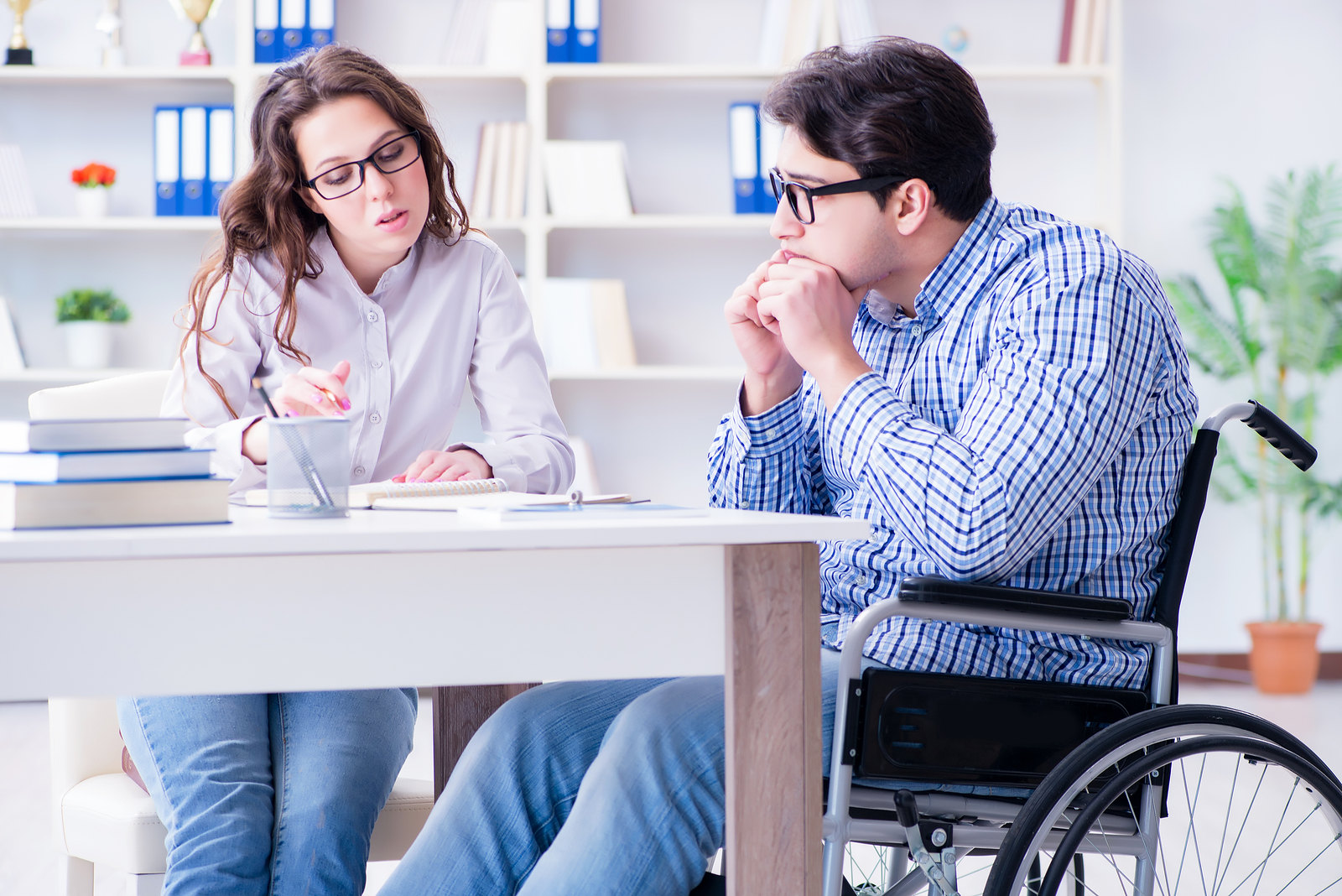 Image presenting a man on a wheelchair studying with his peer.